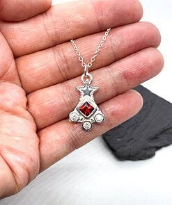 Hand holding a silver star pendant with a red gem and three smaller white gems on a silver chain.