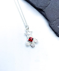 Silver necklace with a star pendant featuring a central red gem and four small clear gems, displayed on a white background.