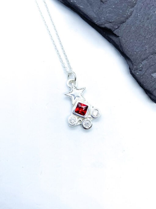 Silver necklace with a star pendant featuring a central red gem and four small clear gems, displayed on a white background.