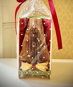 Gift-wrapped Christmas tree made from folded book pages, adorned with colorful decorations and a red bow, inside clear plastic.