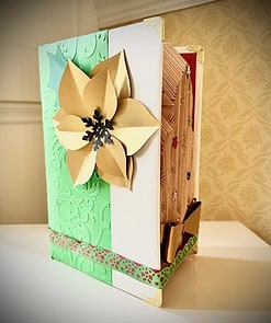 Decorative handmade card featuring a large gold flower, green embossed paper, and a colorful patterned border, standing on a table.