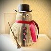 Snowman crafted from folded book, adorned with a red ribbon, buttons, black top hat, and holding a small broom.