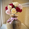 Bouquet of red, white, and pink roses in a vase made from a folded book, adorned with a lavender ribbon and a butterfly decoration.