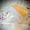 A mannequin head with a knitted beanie featuring a yellow top and white folded brim, set against a floral wallpaper background.