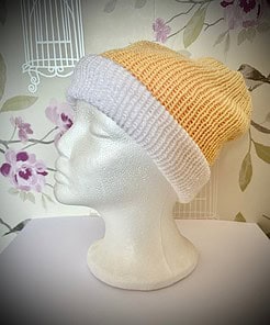 A mannequin head with a knitted beanie featuring a yellow top and white folded brim, set against a floral wallpaper background.