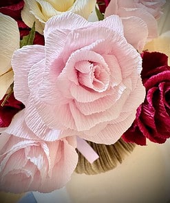 Close-up of a bouquet of paper flowers in soft pink, cream, and red hues with intricate, textured petals.