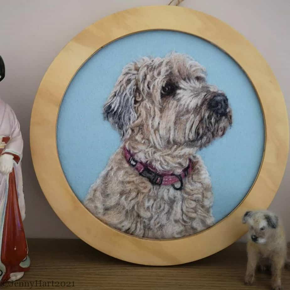 Circular embroidery of a scruffy dog with a pink collar, displayed with a small dog figure and a figurine in traditional clothing.