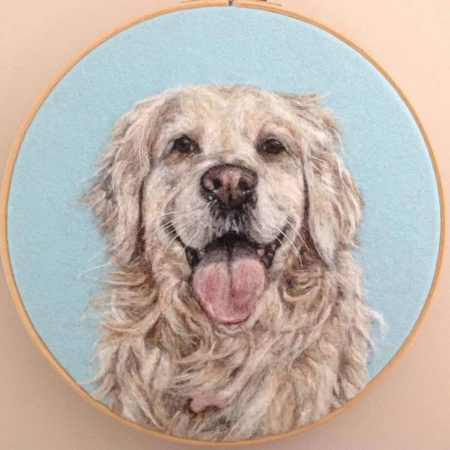 Embroidered portrait of a happy Golden Retriever on a light blue background, framed in a round wooden embroidery hoop.