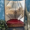 An open book with folded pages spelling "Family," placed on top of three other books, against a blue textured background.