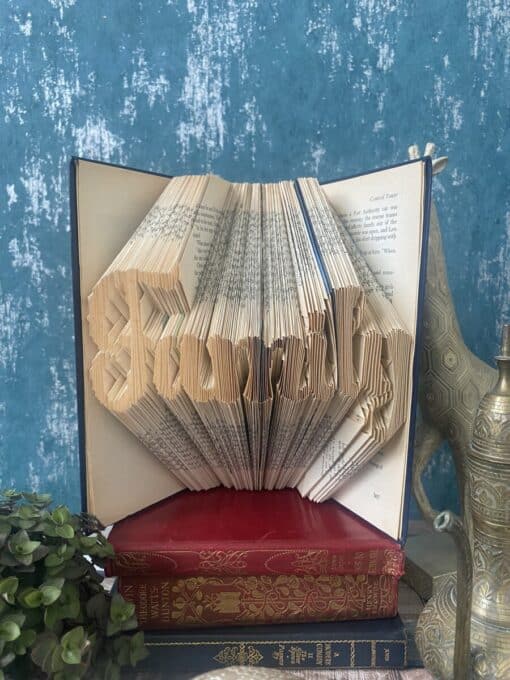 An open book with folded pages spelling "Family," placed on top of three other books, against a blue textured background.