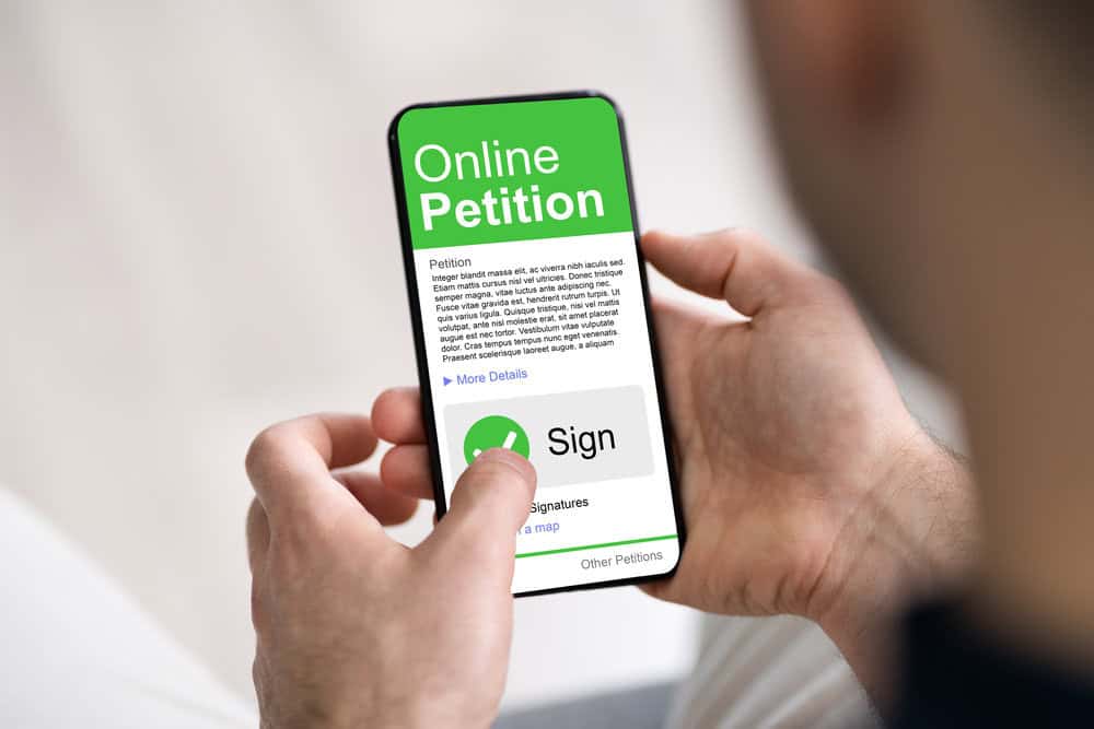 Person holding a smartphone displaying an online petition with buttons to view more details or sign.