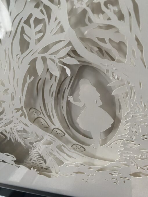 Silhouette of a girl holding an object, surrounded by intricate cut-out designs of trees and leaves, creating a whimsical scene.