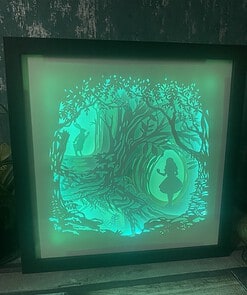 Shadowbox art featuring a green illuminated forest scene with two silhouetted figures, a girl in a dress and a man holding a staff.