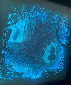 Silhouette of a girl and a rabbit in a forest made from layered paper art, illuminated with blue backlighting.