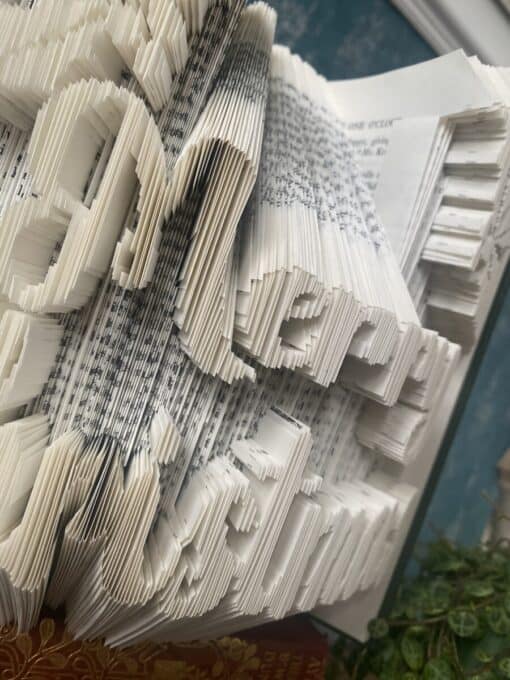 Folded pages of a book spelling "Merry Christmas" in a decorative 3D style, set against a blurred background.