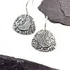 Silver earrings featuring a textured crescent moon and foliage design, placed on a white surface with gray slate accents.