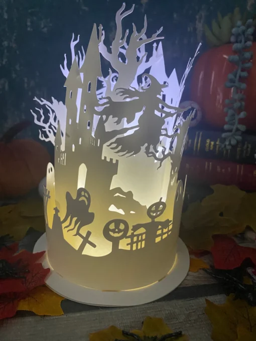 Halloween-themed paper lantern with cut outs of a witch, ghost, pumpkins, and a haunted castle, lit from within.