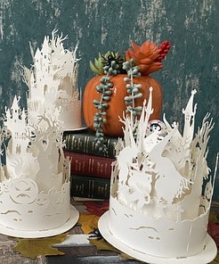 Halloween paper lanterns featuring intricate witch silhouettes on a table with autumn leaves and a pumpkin.