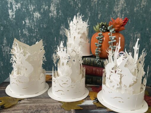 Halloween paper lanterns featuring intricate witch silhouettes on a table with autumn leaves and a pumpkin.