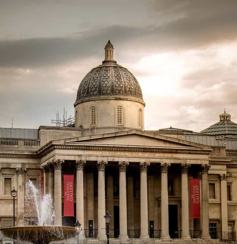 Exterior view of The National Gallery in London with its dome, classical columns, and a fountain in the foreground.