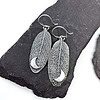 Silver leaf-shaped earrings with intricate vein patterns and crescent moon details, displayed on dark stone slabs.