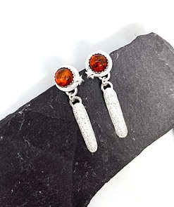 Silver drop earrings with round amber stones and star accents, displayed on a dark slate background.