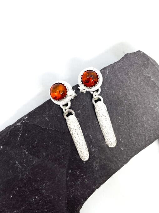 Silver drop earrings with round amber stones and star accents, displayed on a dark slate background.