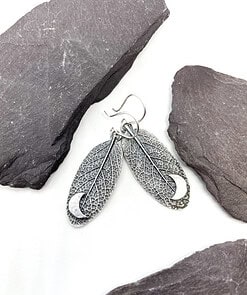 Silver leaf-shaped earrings with intricate vein details and a crescent moon pendant, displayed on dark gray stones.