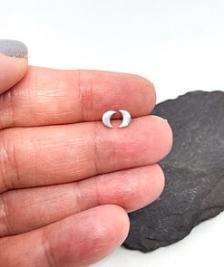 Close-up of a hand holding a small crescent moon-shaped silver stud earring, with a dark rock background.