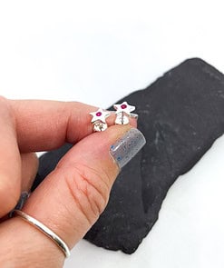 Fingers holding star-shaped silver earrings with pink gemstones against a dark stone background and white surface.