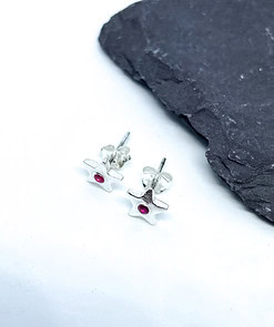 Silver star-shaped stud earrings with red center stones on a white surface, next to a piece of black slate.