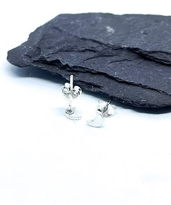 Small silver crescent moon stud earrings displayed on a textured black rock surface.