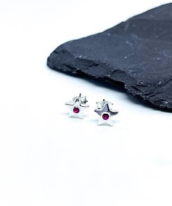 Silver star-shaped earrings with small pink gemstones in the center, placed on a white surface near a black slate.