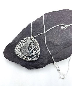 Silver necklace with a crescent moon and leaf pattern pendant, displayed on a black slate background.