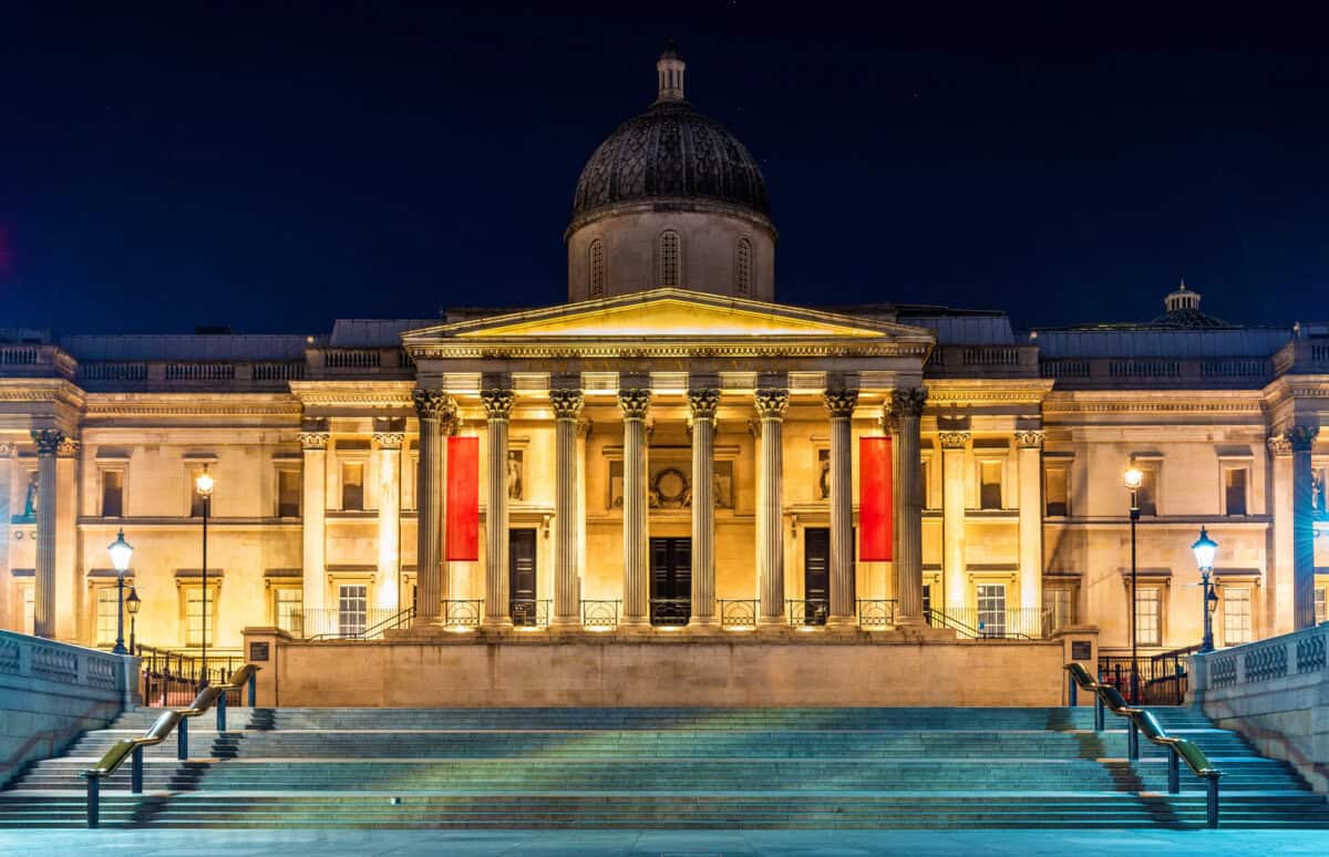 Illuminated building with columns and a dome, seen at night with steps leading up and lampposts on either side.