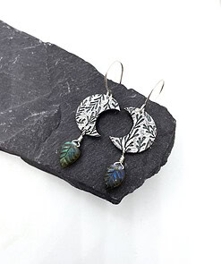 Oxidized silver earrings with floral patterns and leaf-shaped labradorite dangles, displayed on a dark stone surface.