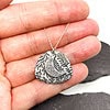 A hand holding a silver pendant with a crescent moon and leaf design, on a silver chain, against a dark background.