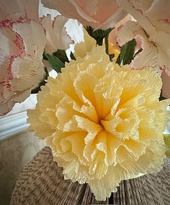 Yellow crepe paper flower surrounded by pink and white flowers, set on a background of folded book pages.