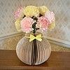 Paper flowers in a vase made from folded book pages, placed on a wooden table against a patterned wallpaper.